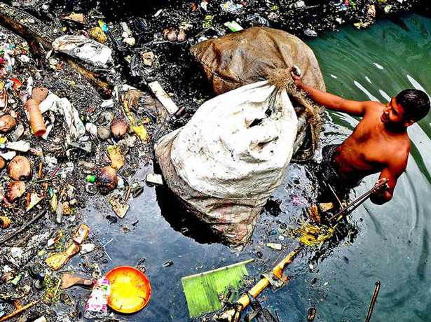 Un recogedor de basura se sumerge hasta la cintura en el agua de un canal de Kochi (India). Foto: © C-HED/Baiju Koduvally